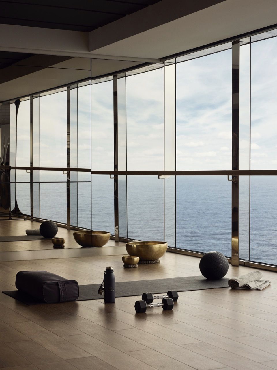 Gymnastikmatte, Hanteln und Klangschalen vor bodentiefen Fenstern auf einem Schiff mit Blick aufs Meer.